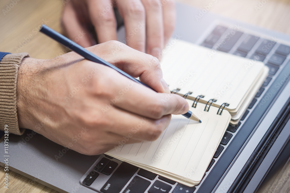 Poster a man's hand is caught in close-up, busily writing in a notepad on a laptop, while the background is