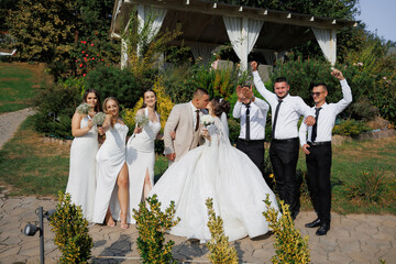 Fototapeta premium A group of people are posing for a picture, with a bride and groom in the center. The bride is wearing a long white dress and the groom is wearing a tie. The group is standing in front of a gazebo