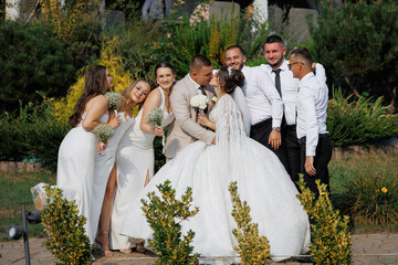 A bride and groom are surrounded by their wedding party, posing for a picture. The bride is wearing...