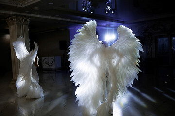 Two people dressed in angel wings are dancing in a dark room. Scene is mysterious and ethereal