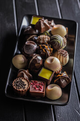 Mix of chocolate pralines on plate on black table.