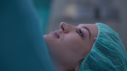Close-up of a woman lying on the operating table with a serene expression, wearing a surgical cap and draped in blue cloth. Concept of childbirth, cesarean section, maternity care, medical procedures