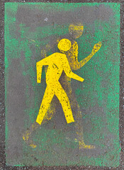 Pedestrian walking paint stencil on sidewalk. A smaller person has been painted over a faded larger...