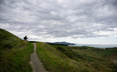 Tramper sitting on the bench, looking at the views of Castlepoint. Wairarapa. New Zealand.