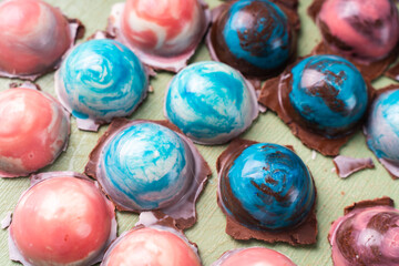Assorted multi-colored homemade chocolates. Modern hand-painted chocolates on a white plate on a blue background. Product concept for chocolatier. Selected focus