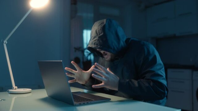 Frustrated hacker shows failure in dark room with laptop on table.