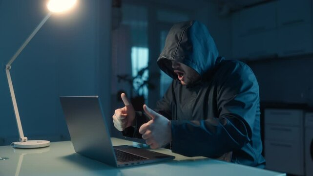 A happy hacker celebrates online victory, working in a dimly lit room.