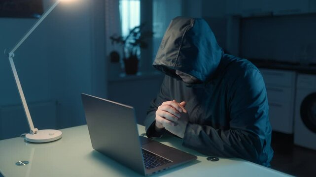 Anonymous hacker typing rapidly on a laptop in a dim home office.