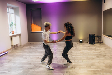 Slim young man and woman practicing salsa dance in training hall during group dancing classes