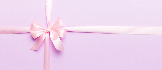 Top view of purple ribbon rolled and pink bow isolated on colored background. Flat lay with copy...