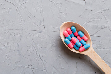 Vitamin capsules in a spoon on a colored background. Pills served as a healthy meal. Red soft gel vitamin supplement capsules on spoon