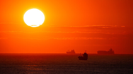 Silhouettes of cargo ships on the horizon at sunset and sunrise