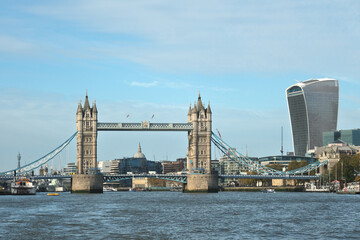 Obraz premium Iconic Tower Bridge in London over the River Thames with the city skyline, including modern skyscrapers like the Walkie Talkie building, under a clear blue sky. Historic architecture meets modernity