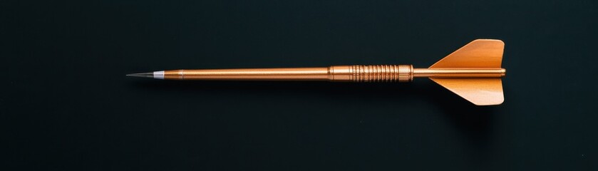 Fototapeta premium A sleek, golden dart lies horizontally on a dark surface, showcasing its streamlined design and sharp tip.