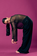 Fashion asian woman in sheer top bending over with hands on knees, head tilted on purple background