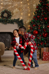 Happy asian children playing with big sweet lollipop candies in cozy room decorated with christmas tree and garlands, merry christmas