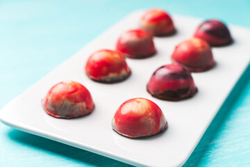 Assorted multi-colored homemade chocolates. Modern hand-painted chocolates on a white plate on a blue background. copyspace.Product concept for chocolatier. Selected focus.