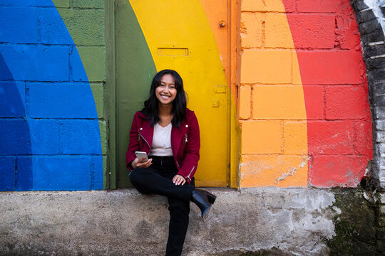 Smiling woman sitting with smart phone in front of multi colored door