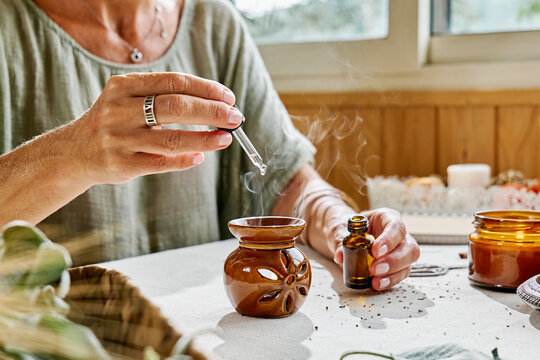 Woman dropping aroma oil through dropper in diffuser