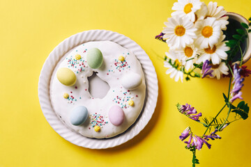 Easter doughnut decorated with chocolate eggs near flowers over yellow table