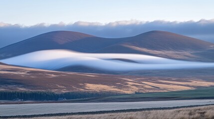 Fototapeta premium Fog drifts between rolling hills at dawn.