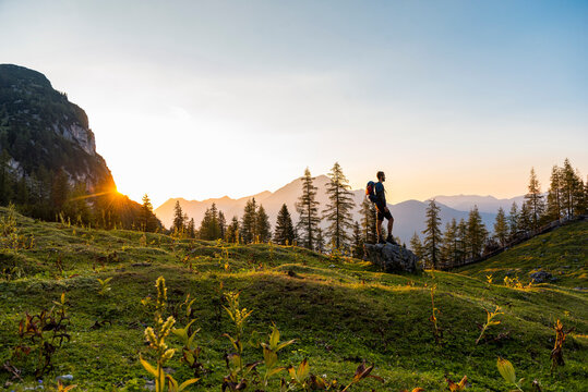 Austria, Tyrol, Hiker with backpack standing on rock, watching sunset