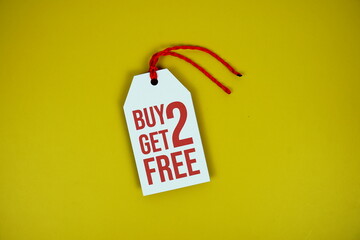 Buy 2 Get 2 Free on price tag with wooden clothes hanger top view on yellow background