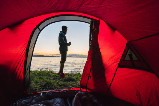 Man camping in Estonia, standing in front of tent, watching sunset - Powered by Adobe