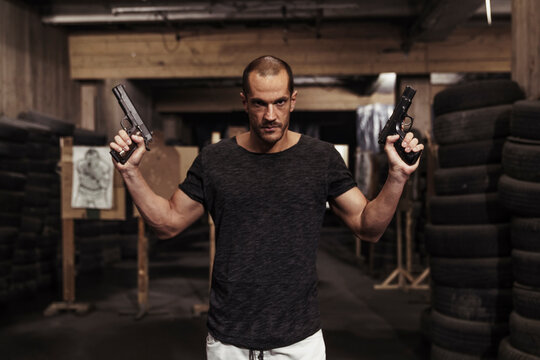 Portrait of man posing with two guns in an indoor shooting range