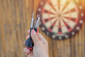 Close up shot black and red darts arrows in women hand over dartboard game
