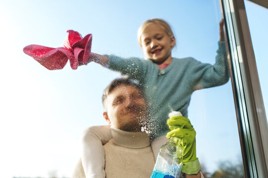 Man carrying daughter on shoulders and cleaning window