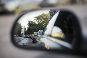 Rearview Mirror Perspective of Urban Street with Parked Cars and Trees