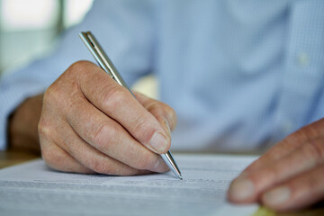 Hands of senior man filling form with pen at table