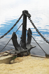 Large Iron Anchor and Chain on Sandy Shore Near Calm Waters of Lake