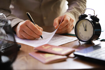 Close-up of Person Signing Document with Passport and Clock on Desk, Emphasizing Urgency and Travel