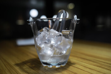 Clear Glass Ice Bucket with Ice Cubes on Wooden Table in Dimly Lit Room