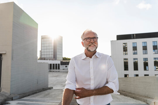 Mature man standing on roof of a high-rise building, rolling up sleeves