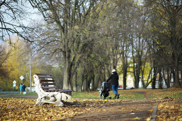Autumn Park Bench and Walking Parent with Stroller in Scenic Fall Setting