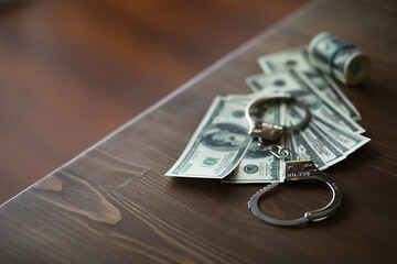 Handcuffs on Wooden Table with Rolled Dollar Bills Symbolizing Financial Crime and Corruption