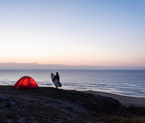 Young woman camping on the beach, carrying surfboard at night