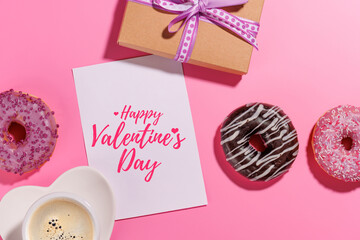 A festive flat lay featuring vibrant donuts with colorful toppings and a blank greeting card on a pink background