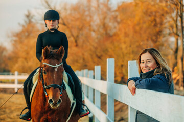 Happy mother with daughter practicing horseback riding in autumn