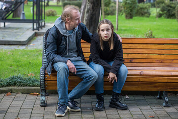 Tired child girl with father sitting on the bench, outdoor portrait