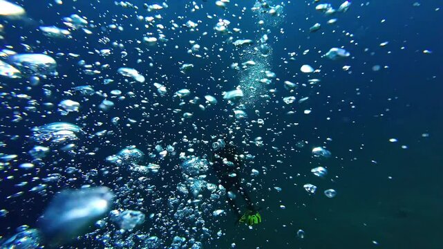 A Diver Releases Streams of Air Bubbles While Descending Into the Deep Blue Sea - Underwater Shot