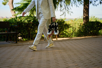 Close-up of man in striped suit carrying roller skates while walking in sunny park