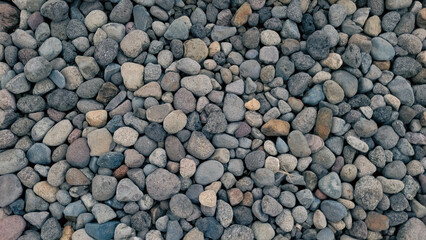 Close-up of a collection of small, rounded stones with varying shades of gray, beige, and brown. The texture and natural colors create a rustic and organic feel, ideal for backgrounds, nature themes.