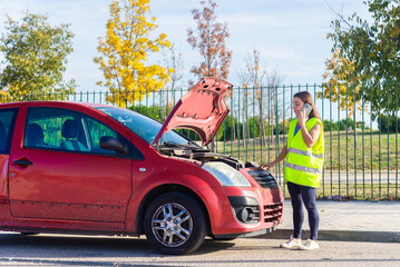 Woman in safety vest calling for assistance by broken car