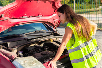 Woman in safety vest checking car engine by roadside