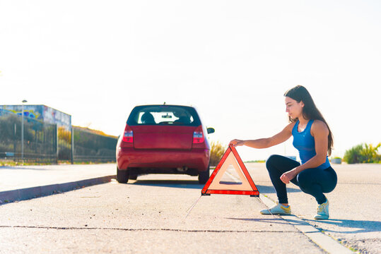 Young woman setting up warning triangle after car breakdown