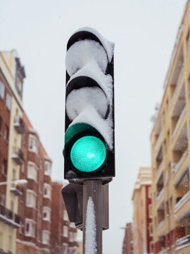 Green traffic light covered in snow during city snowfall